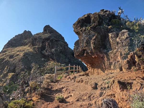 Eroded volcanic rock forms an overhang beside the ridge path protected by a handrail.