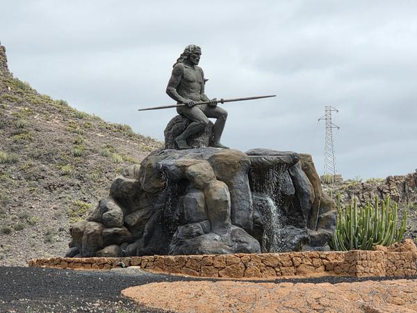 Statue of Mencey Guanche Tinerfe with waterfall in a volcanic landscape.