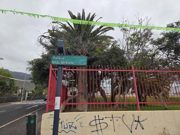 Entrance sign of Parque Santa Ursula surrounded by palm trees and red fencing.