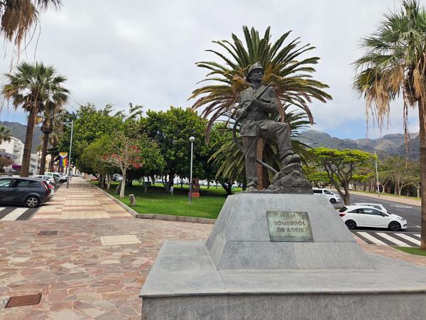 Bronze statue honoring Adeje's firefighters, placed in a palm-lined plaza.