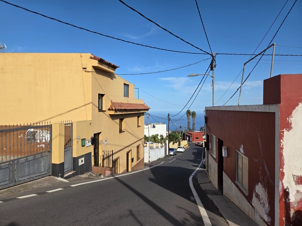 Calle de Aguamansa en pendiente con casas de colores y vistas al océano al fondo.