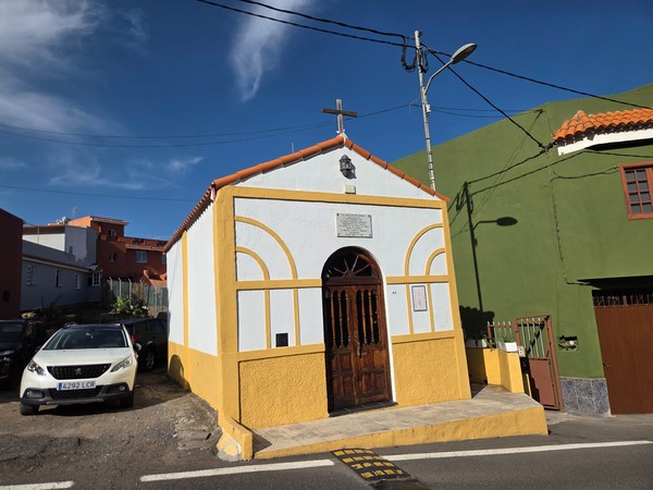 Pequeña capilla de fachada blanca y amarilla en una calle de Aguamansa.