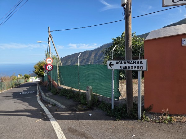 Cartel direccional hacia Aguamansa y Bebedero junto a la carretera con el mar al fondo.