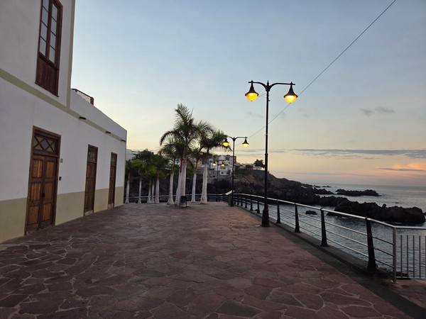 Palm trees and classic streetlamps on the Alcalá seafront promenade overlooking the Atlantic at sunset.