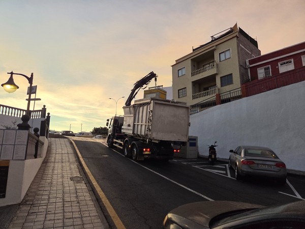 Service truck on a sloping street in Alcalá with mixed apartments and sunset sky.