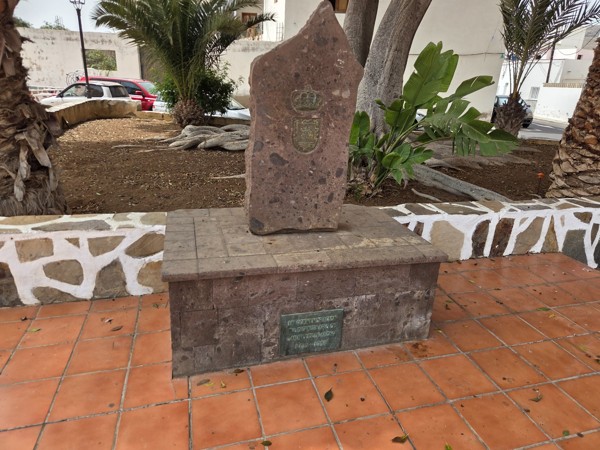 Stone monument on a tiled base with a metal plaque in the plaza of Aldea Blanca.