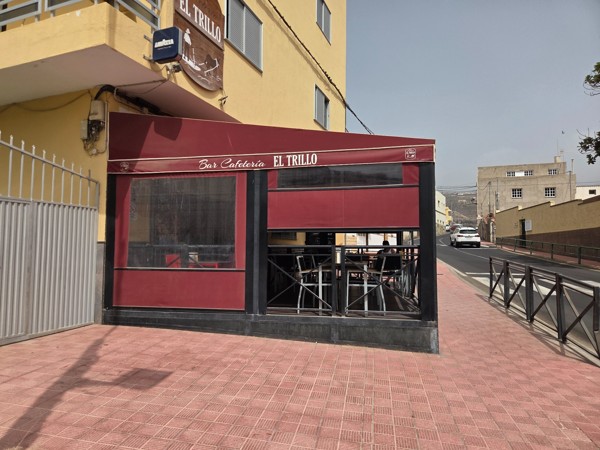 Corner terrace of Bar Cafetería El Trillo in Aldea Blanca with red awning and outdoor seating.