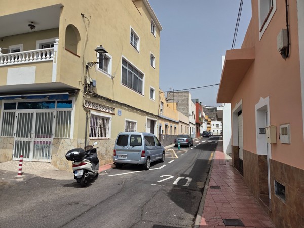 Narrow residential street in Aldea Blanca with low-rise houses and parked cars.