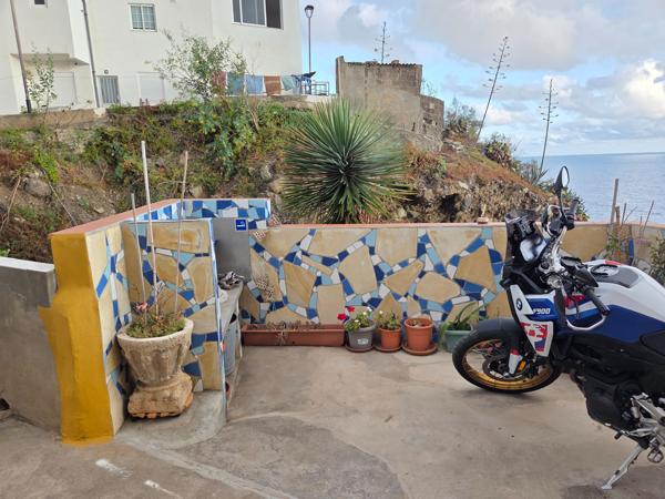 Mosaic-tiled corner terrace with potted plants and a parked motorcycle near the cliff.