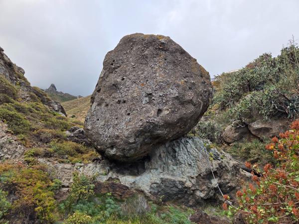 Massive volcanic boulder balanced on a rock formation along a trail in Almáciga.