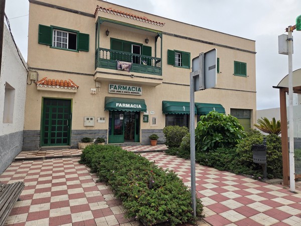 Arico pharmacy building with green awnings and a small plaza in front.