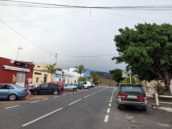 Wide street view in Arico with parked cars and trees leading uphill toward the mountains.