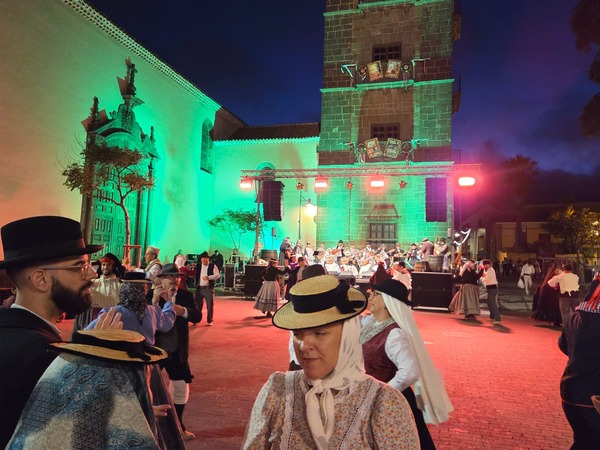 Folk musicians perform onstage in front of La Concepción while the tower glows with coloured light.