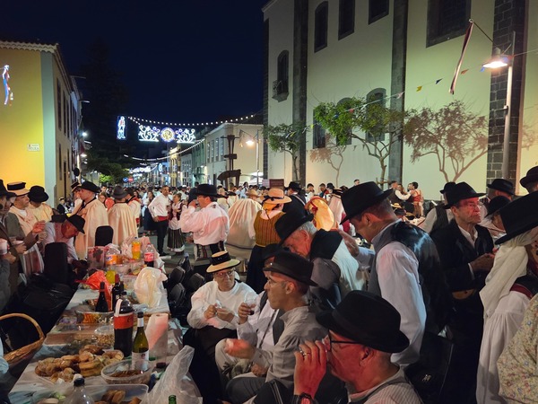 Long tables with food and drinks set along the church wall, with attendees wearing hats, capes and waistcoats.