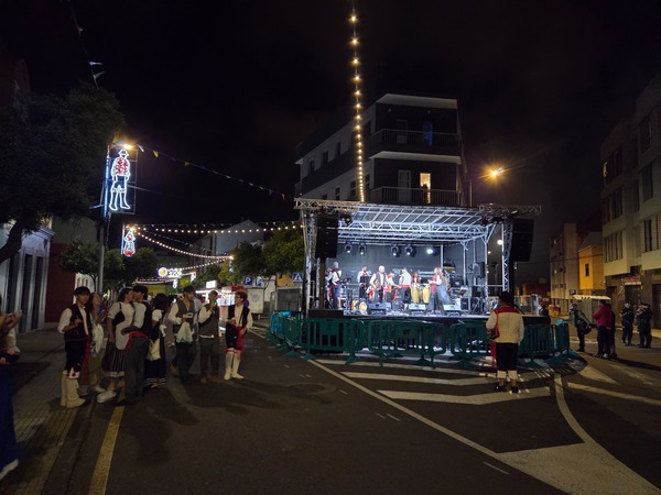 Musicians perform on a secondary street stage with festive lighting and silhouettes of traditional figures.