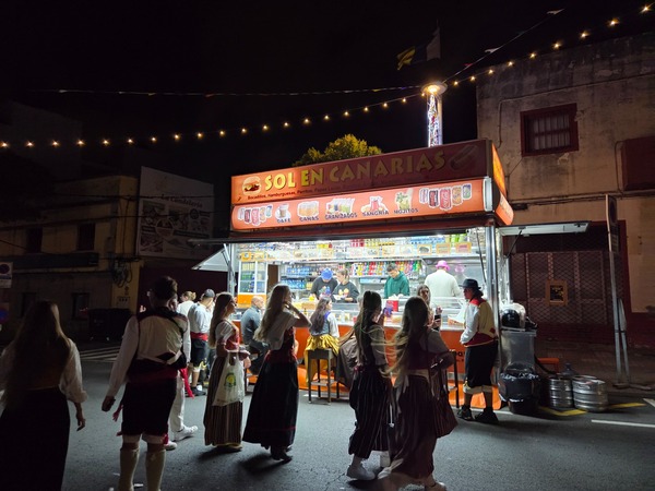 Food stall named 'Sol en Canarias' serving attendees in traditional dress late at night.