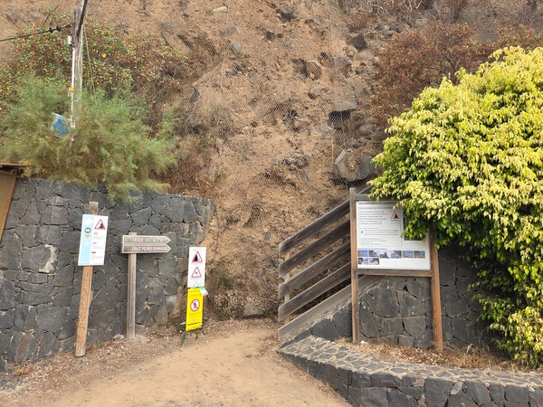 Trailhead of the Barranco Ruiz path with warning signs, stone walls and netting at the entrance near Icod El Alto.