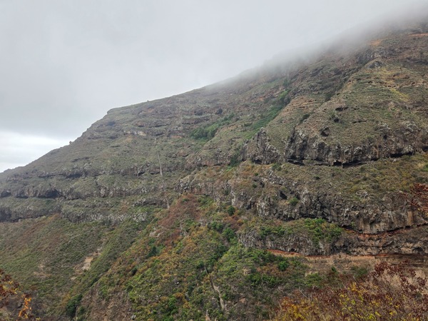 Terraced ledges and natural caves along the steep slopes of Barranco Ruiz under a low cloud ceiling.