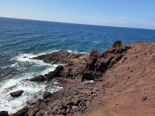 Sharp black rocks and reddish volcanic terrain along the oceanfront near Montaña Bocinegro.