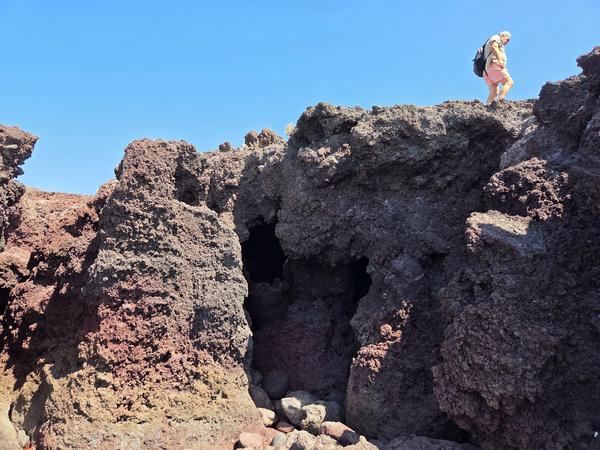 Person hiking above jagged volcanic caves on the coast near Montaña Bocinegro in Tenerife.