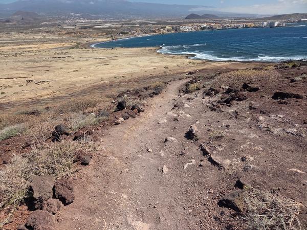 View from Bocinegro trail looking toward the coastline and El Médano town, with ocean waves meeting the shore.