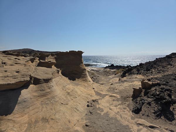Flat, eroded volcanic landscape ending at the sea with stone-lined paths.