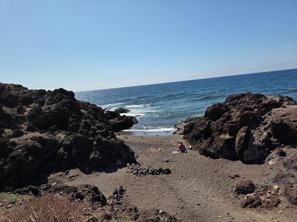 Secluded sandy cove surrounded by dark volcanic rocks with a person sunbathing near the Atlantic shore.
