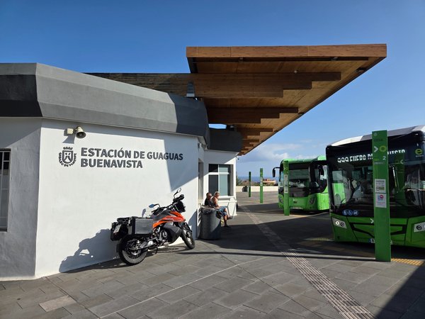 Buenavista bus station with green Titsa buses and waiting area under wooden roof.