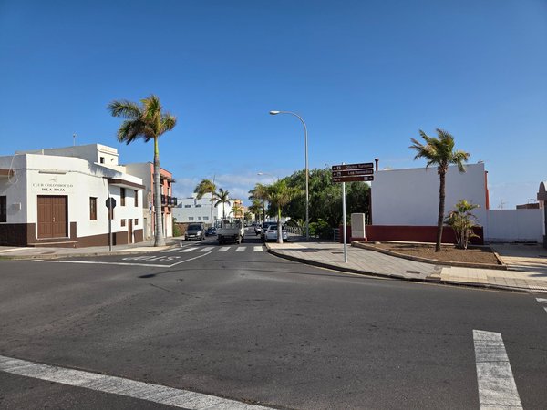 Crossroad view with palm trees, directional signs, and blue sky.