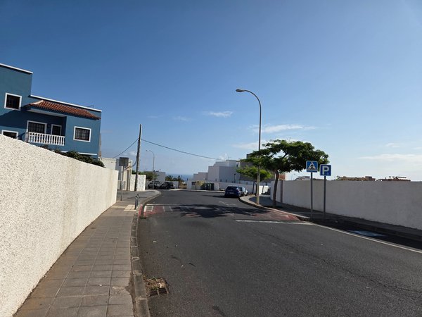 Quiet residential street with blue house and ocean visible in the distance.