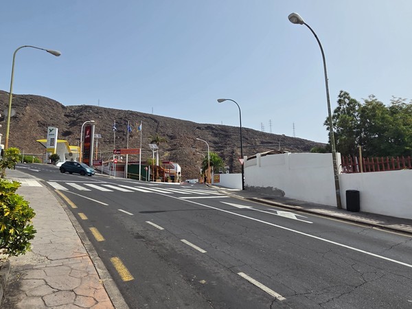 Uphill roadway by a service station with arid hills behind—one of the vehicular access points near Barranco Hondo.