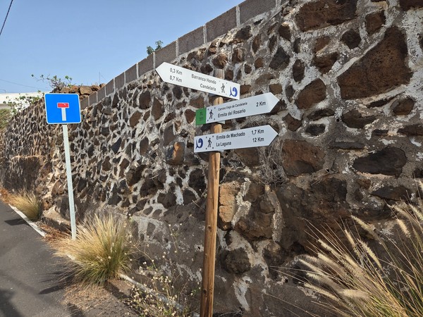 Wooden waymark arrows for the Camino Viejo de Candelaria, indicating nearby places such as Barranco Hondo, Candelaria and La Laguna.