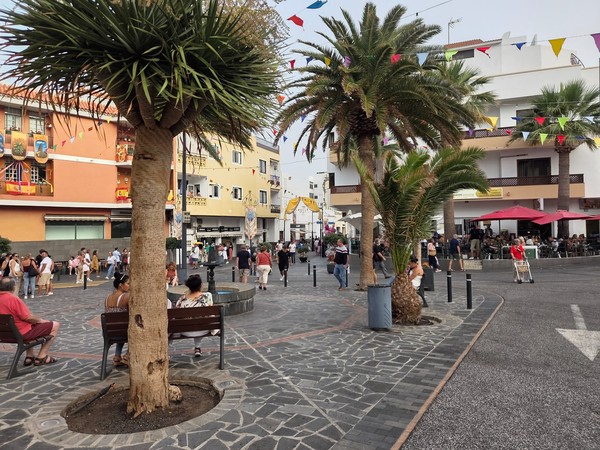 Local square in Candelaria with palms, benches and people gathering under fiesta bunting.