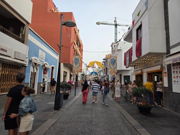 Busy pedestrian street in Candelaria with shopfronts and fabrics draped from balconies for the festival.