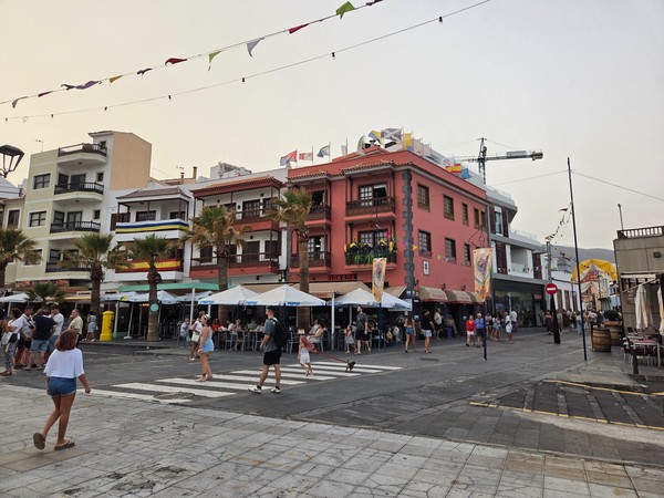 Seafront plaza corner with restaurant terraces and colorful buildings decorated for Candelaria fiestas.