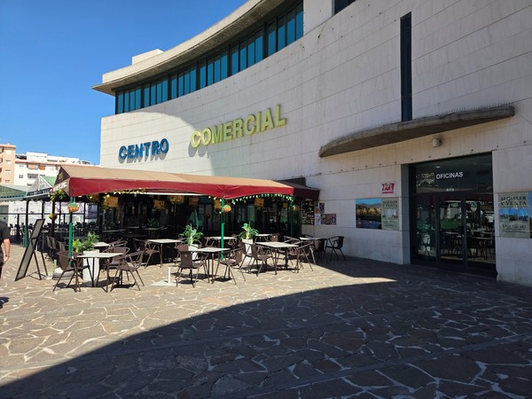 Ground-level façade of Centro Comercial with terrace seating next to the OFICINAS entrance and signage reading Centro Comercial.
