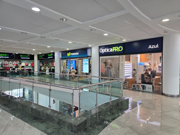 OpticaPRO and Movistar stores side by side on the upper level near the railings.