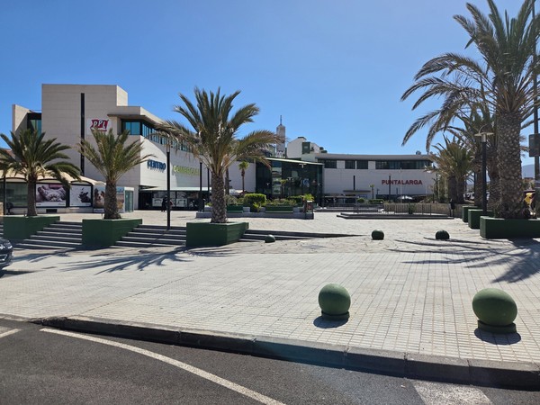 Wide view of Centro Comercial Punta Larga with palm trees and the open plaza in front of the main entrances in Candelaria, Tenerife.