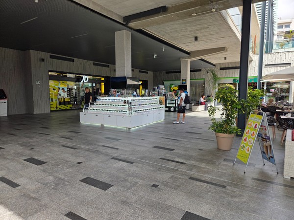 JD storefront and a sunglasses kiosk on a shaded plaza.