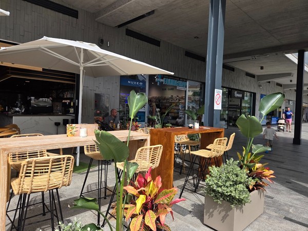 High wooden tables with bar stools and umbrellas on a café terrace.