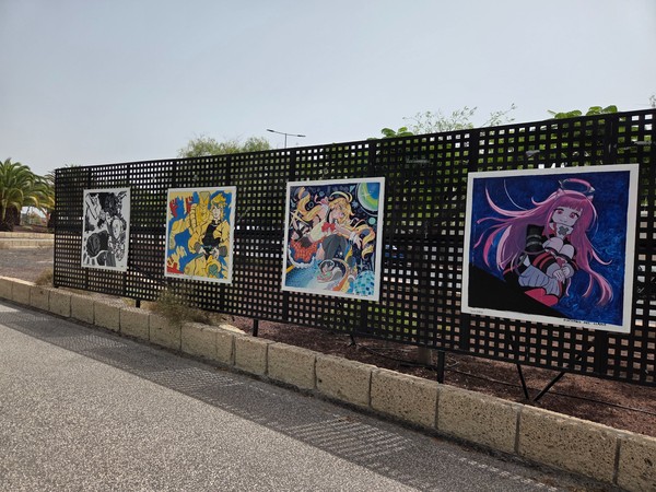 Outdoor exhibition of colorful anime paintings displayed on a fence in La Chafira.
