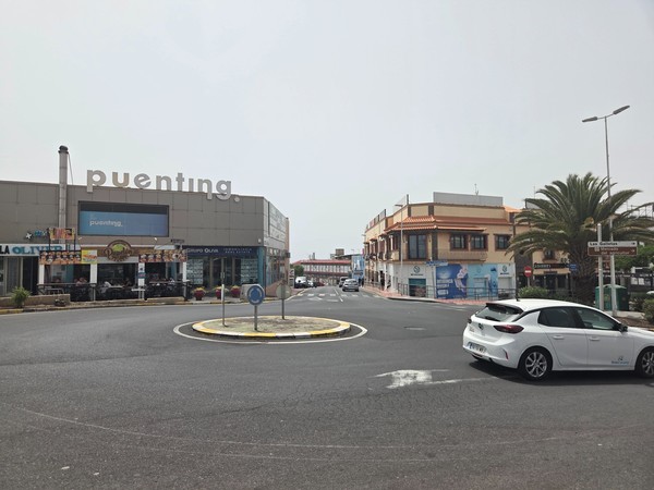 Roundabout with Puenting building, cafés and signage toward Las Galletas.