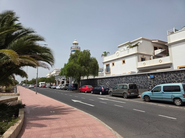 Street view with lighthouse tower and palm sidewalk in La Chafira.