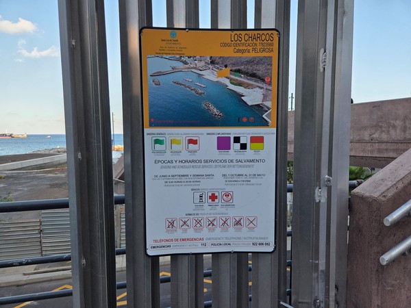 Information sign for Los Charcos showing beach flag colors and seasonal lifeguard schedules.