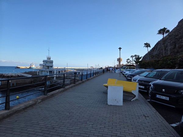 Seafront promenade of Los Charcos with benches, railing and parking along the cliffside.