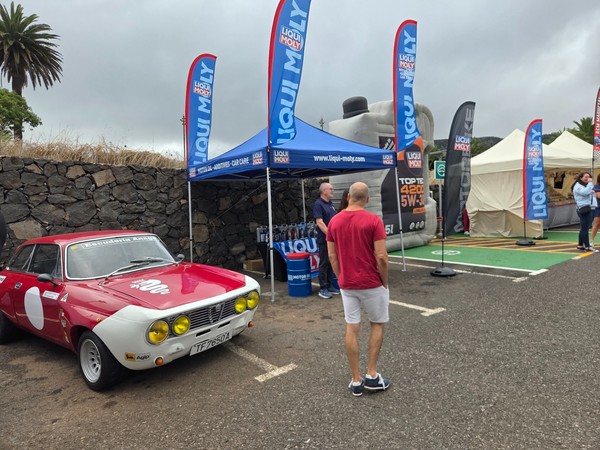 Alfa Romeo club stand with a race-prepared coupe on display, helmets and equipment under white canopies.
