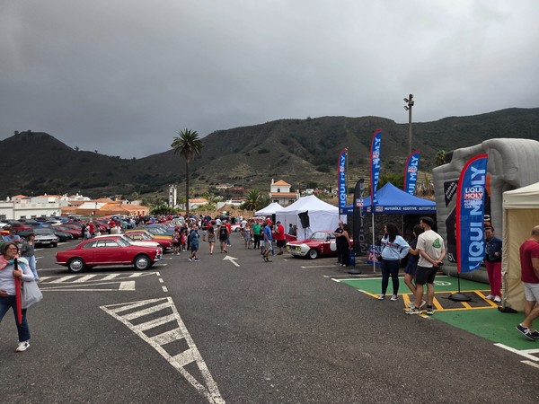 Wide view of the classic car meet in Tegueste with rows of vintage cars, visitor crowds and sponsor tents set against the green hills of Tenerife.
