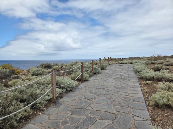 Straight section of rope-lined pathway across low coastal scrub with open sea views at Costa de Acentejo.