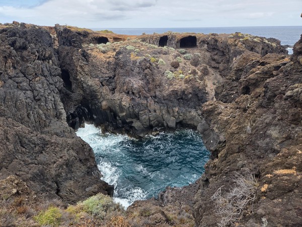 Circular volcanic inlet where waves churn turquoise water in a natural rock pool.