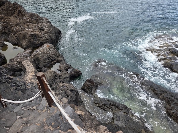 Rock steps with a safety rope descending to tidal pools and clear water on the lava shelf.